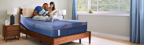 A man and a woman sitting on a posturepedic elite mattress while reading